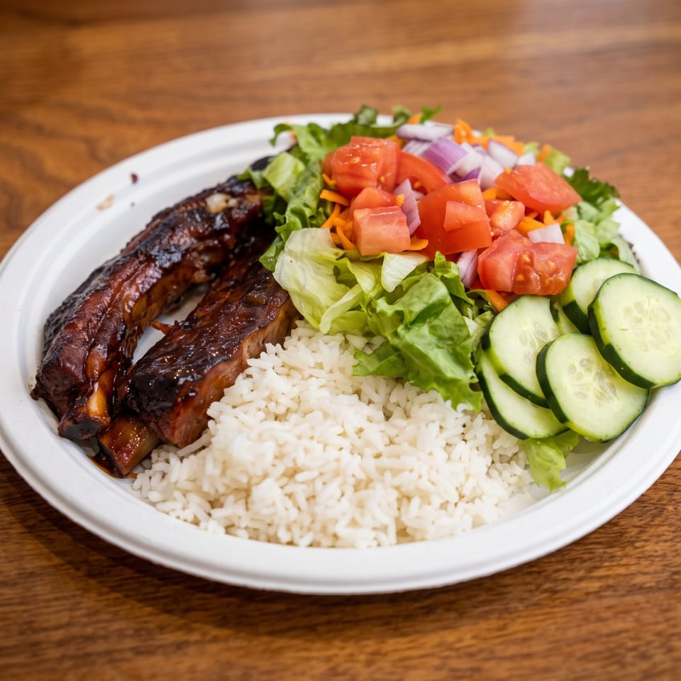 Plate of glazed grilled ribs with white rice, lettuce salad, tomatoes, carrots, onions, and sliced cucumbers on a wooden table.
