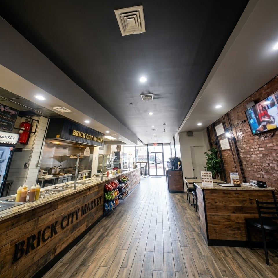 Brick City Market restaurant interior with a counter, displayed snacks, wood flooring, brick walls, tables, and bright storefront entrance.